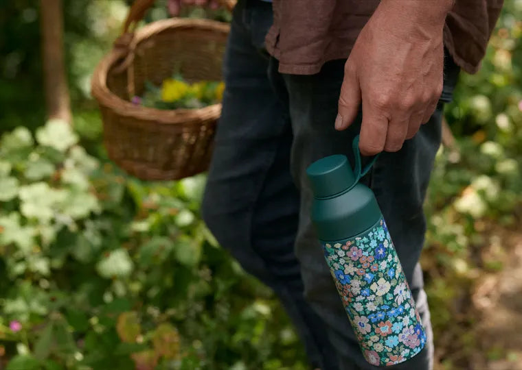 man walking through forest terrain with basket for foraging and Ocean Bottle x Liberty London Morley Blossom water bottle